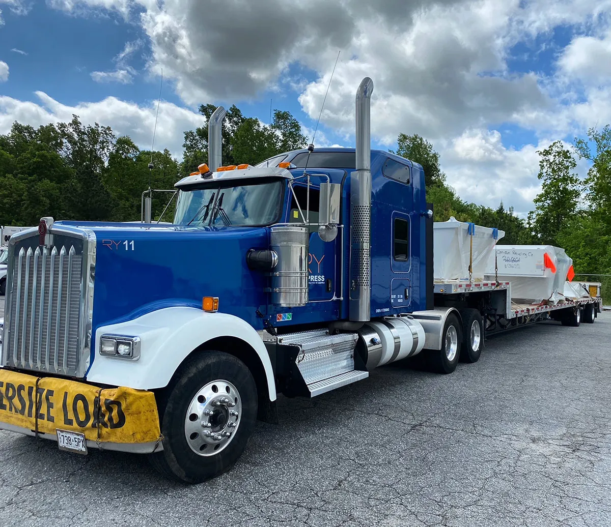 Blue RY11 Kenworth with oversize load banner hauling flatbed cargo