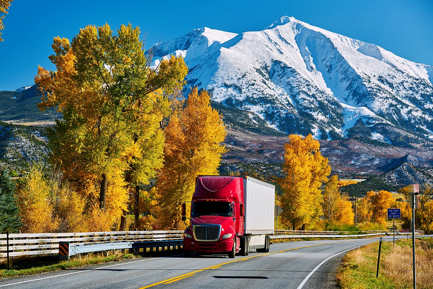 Red semi-truck with white trailer on autumn Colorado highway