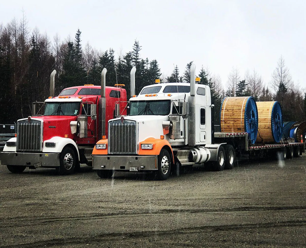 Two Kenworth trucks with cable spools on flatbed