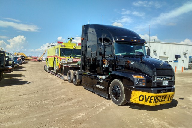 Black RY19 Mack with OVERSIZE LOAD banner hauling yellow fire truck