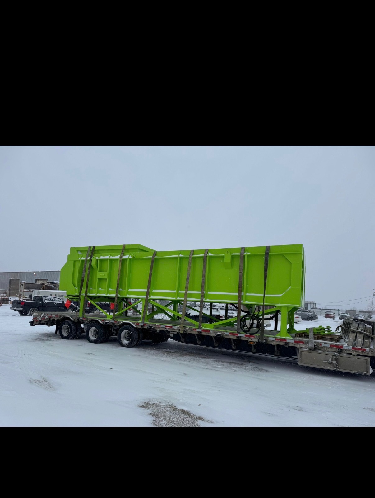Large lime green industrial hopper on flatbed trailer in snowy yard