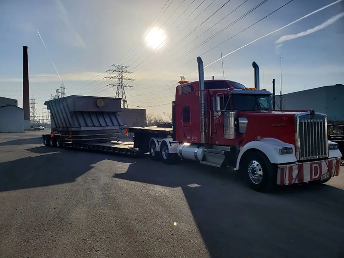 RyXpress Kenworth lowboy hauling industrial equipment at sunset