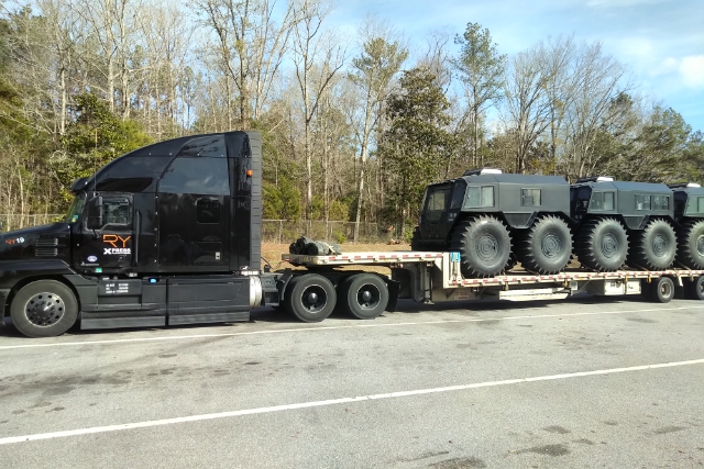 Black RY Mack truck hauling military HEMTT vehicles on flatbed
