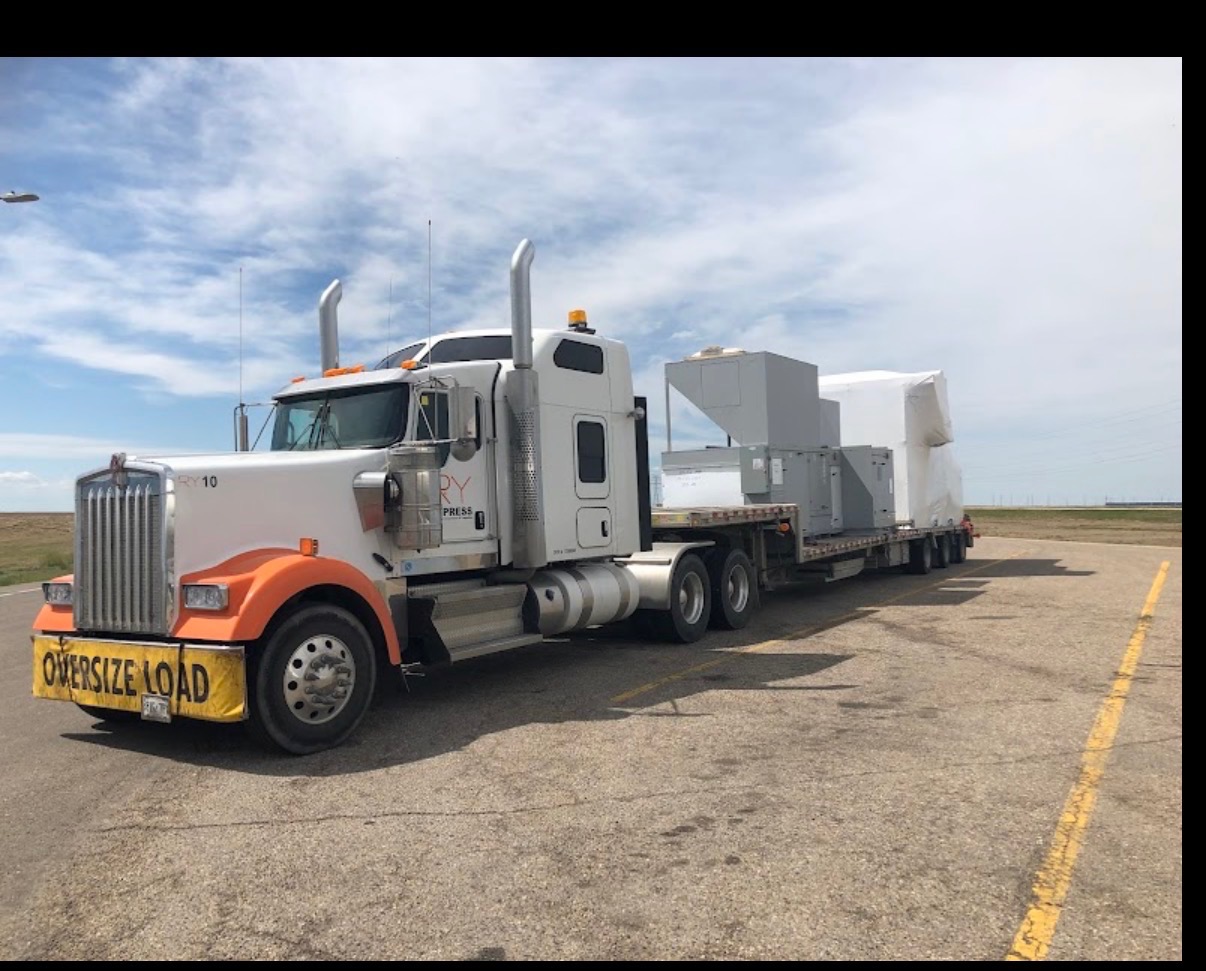 White and orange RY10 Kenworth with oversize load hauling wrapped equipment