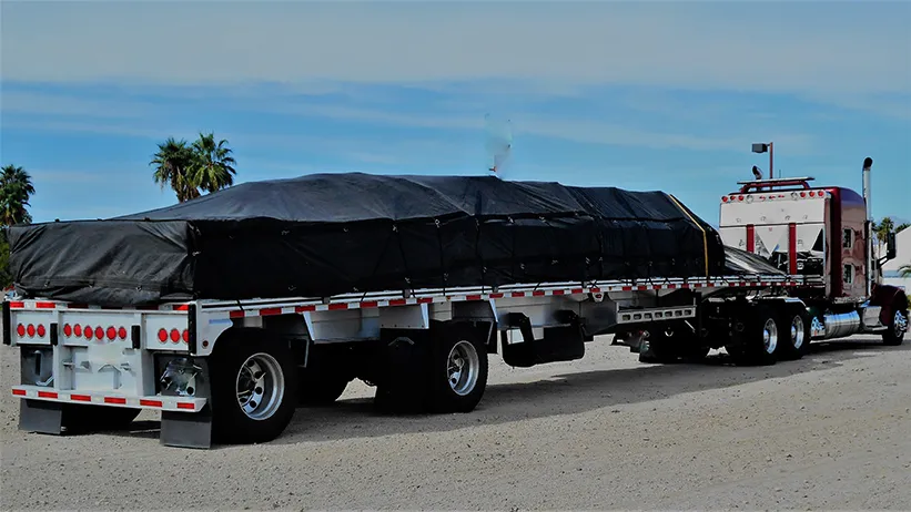 Flatbed semi-truck with black tarped load in desert