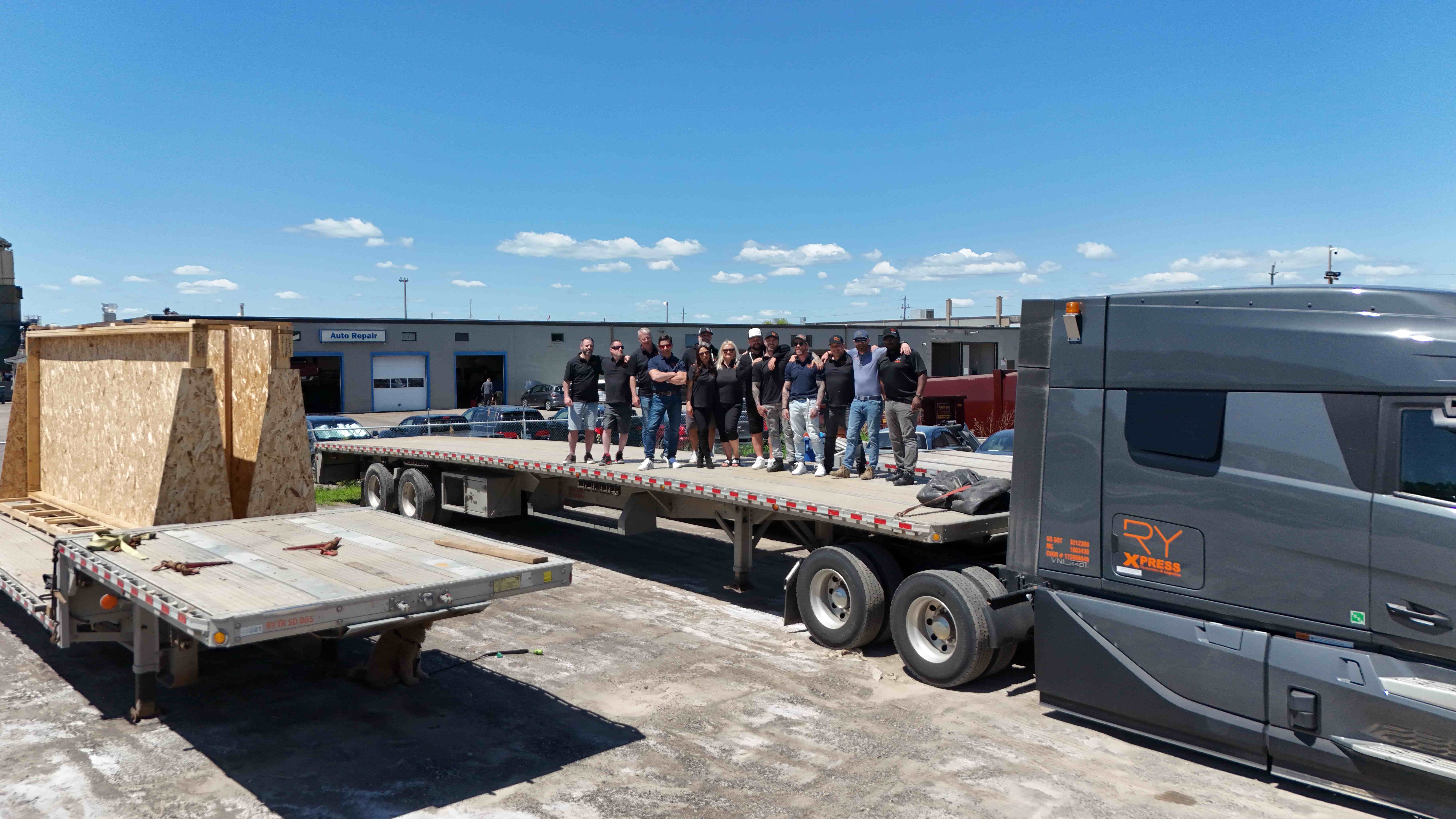 RY Xpress team standing together on a flatbed trailer beside their Volvo VNL