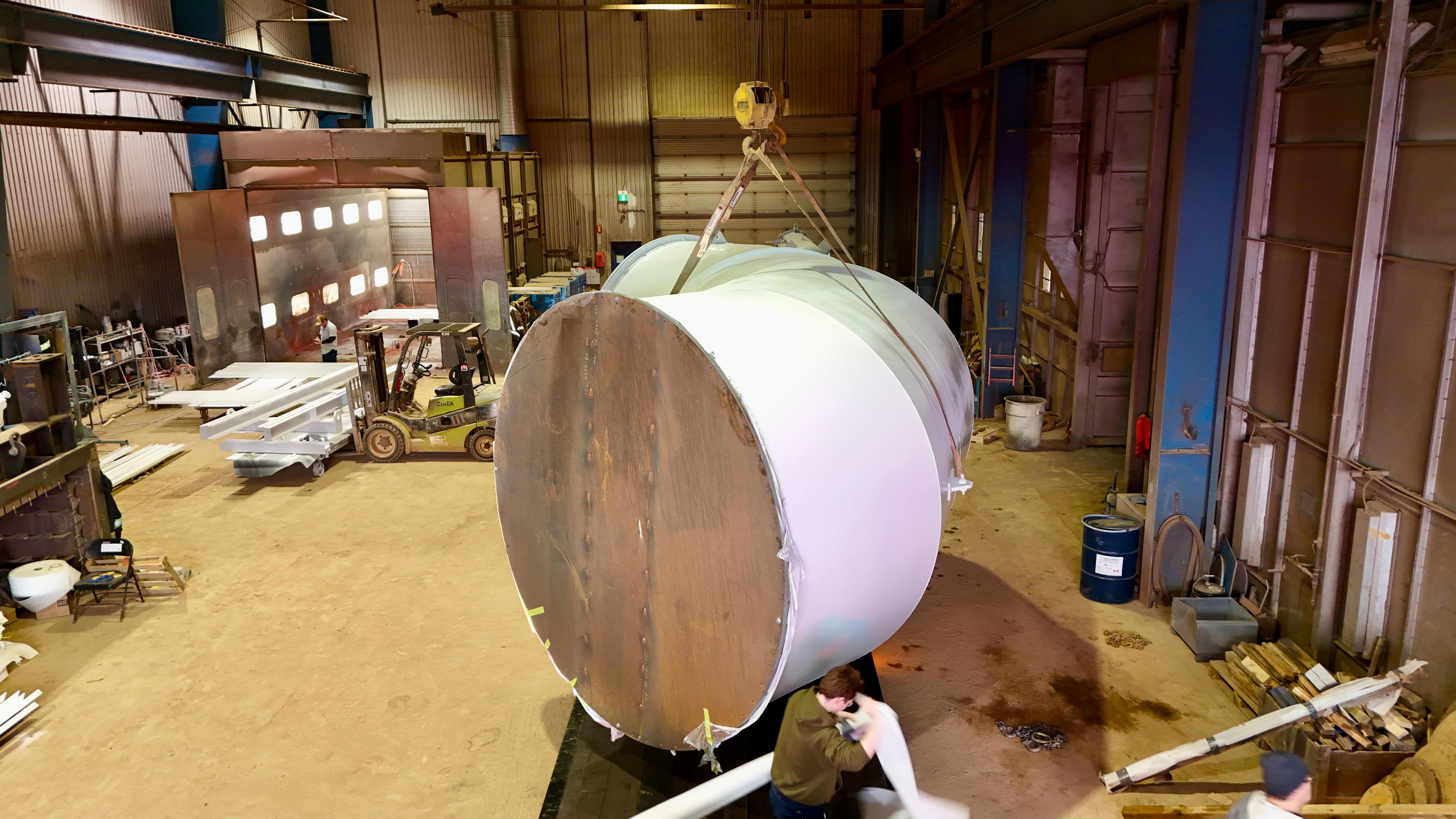 Massive cylindrical tank being lifted by industrial crane in warehouse