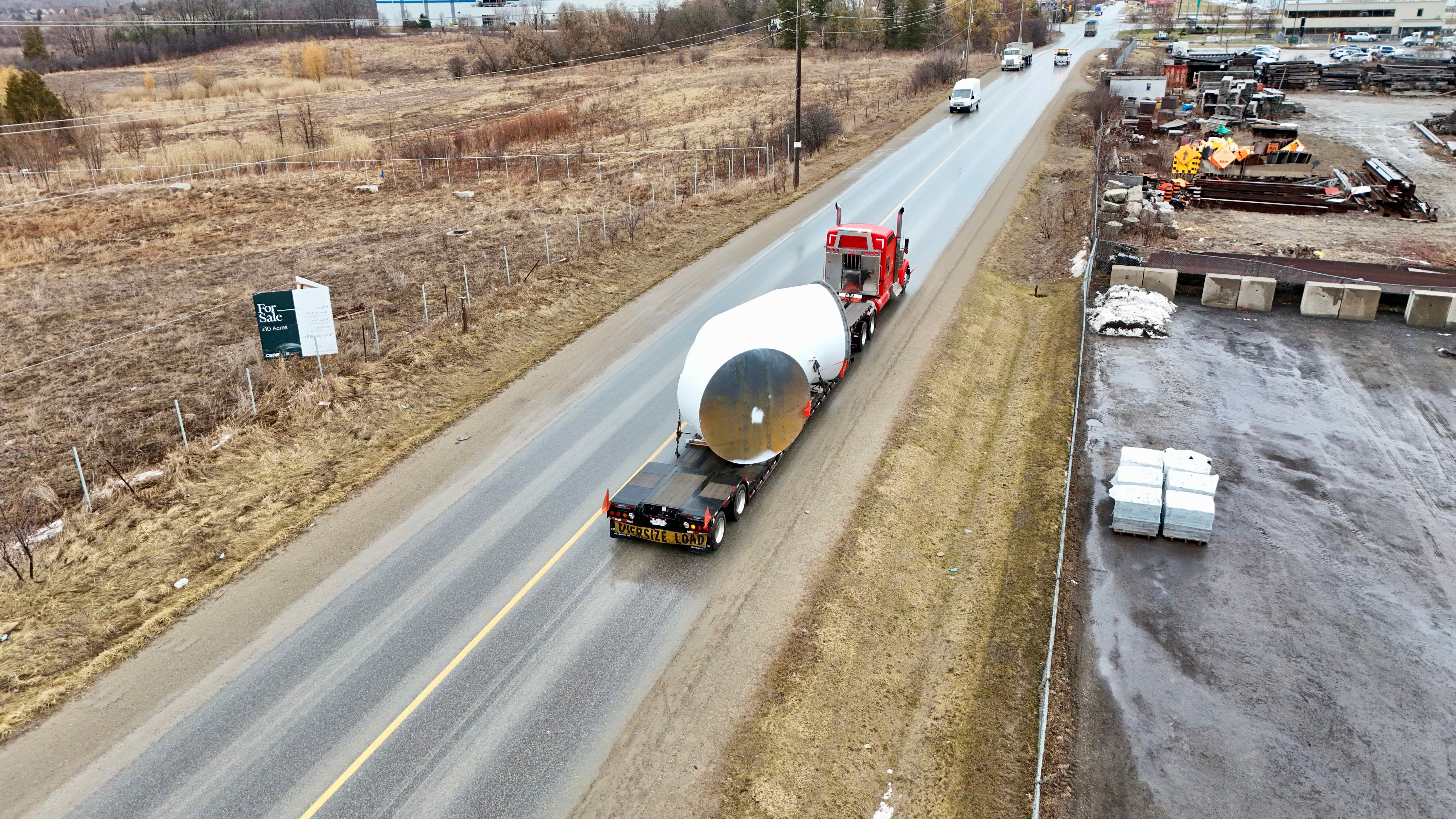 RY red Kenworth hauling oversized cylindrical tank on highway