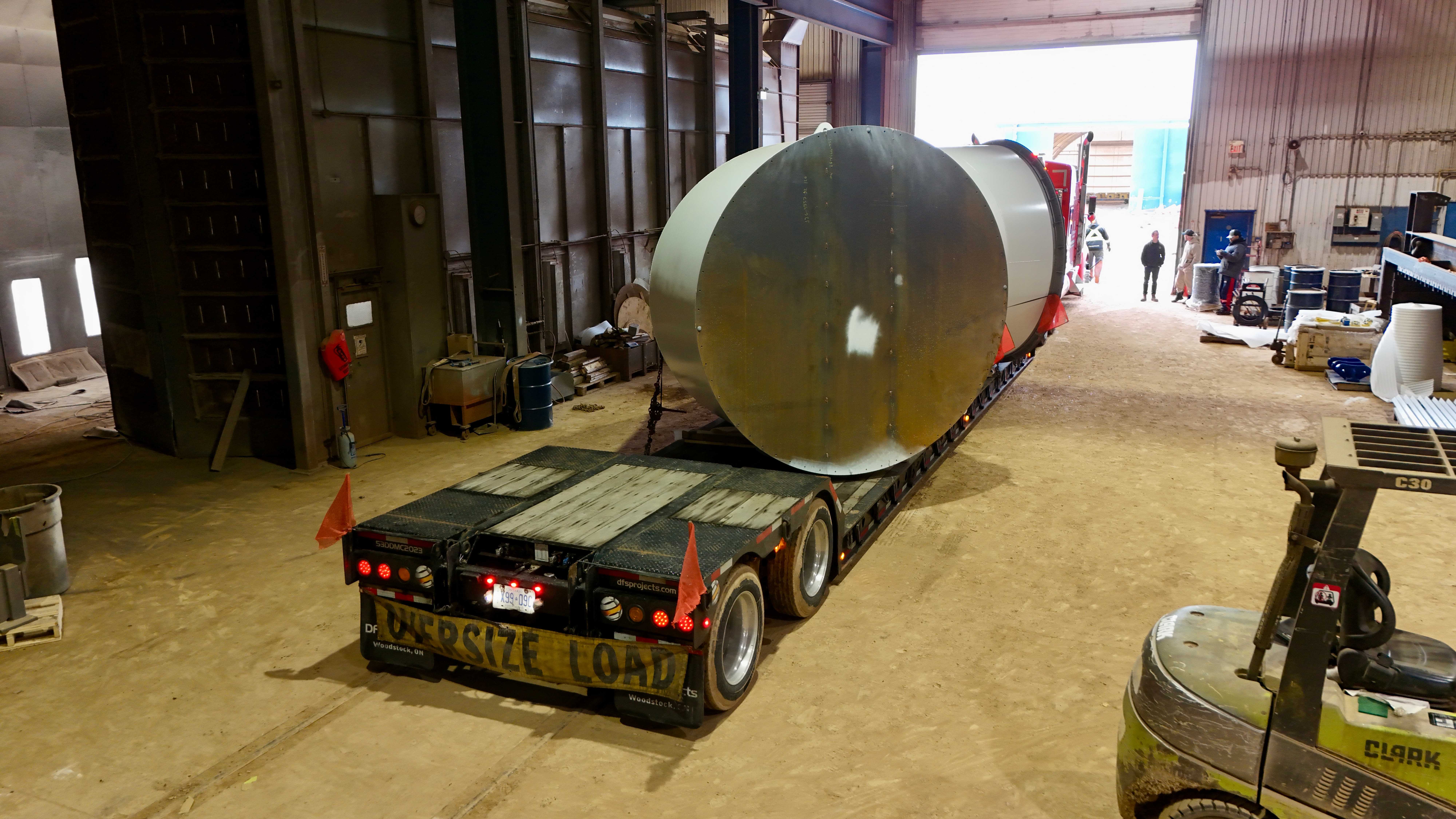 Large cylindrical tank loaded on flatbed with OVERSIZE LOAD banner inside warehouse