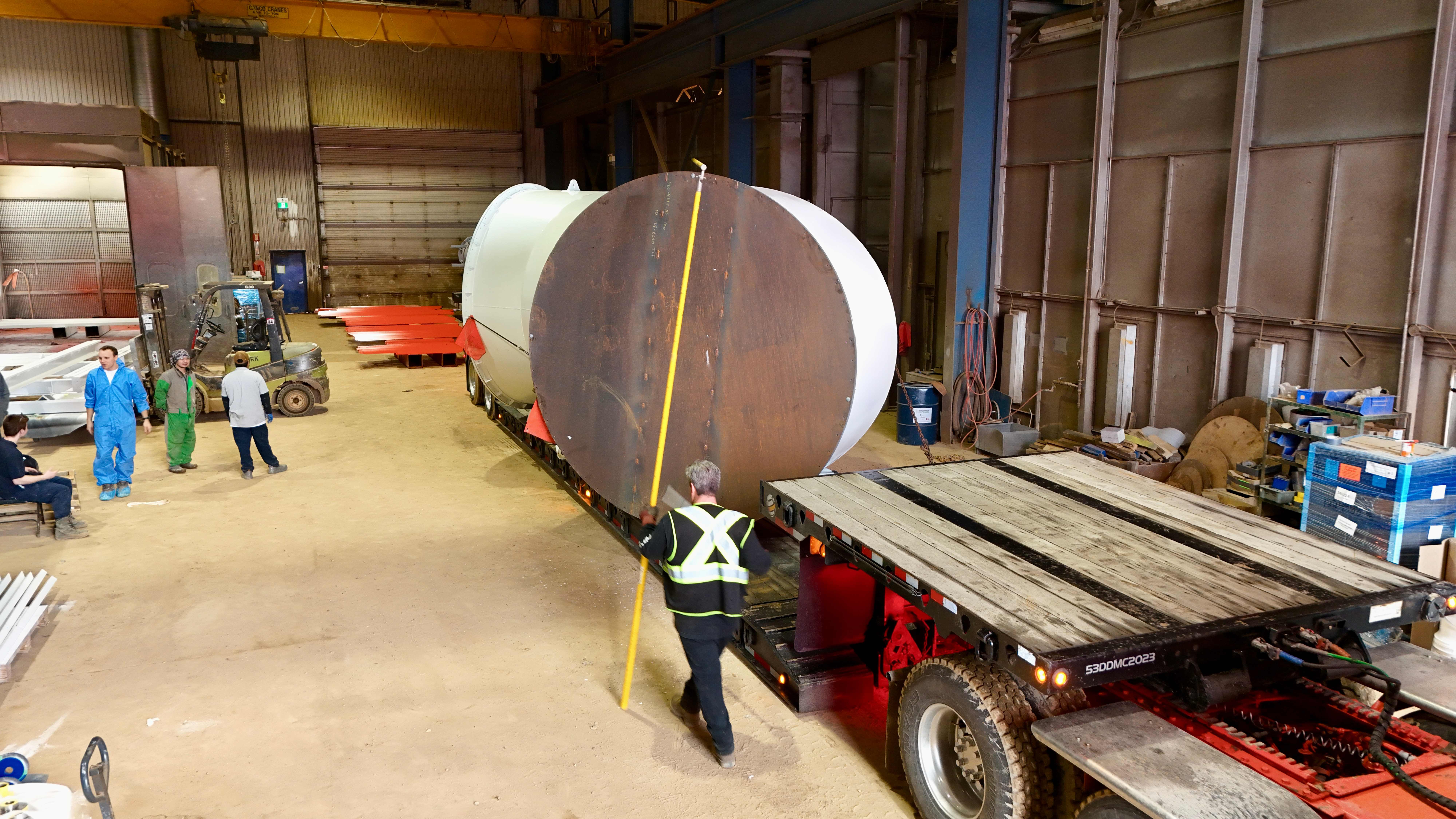 Worker measuring large industrial tank on flatbed trailer in warehouse